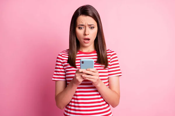 Foto de la joven triste impresionada mirada teléfono boca abierta desgaste casual camiseta aislada sobre fondo rosa — Foto de Stock