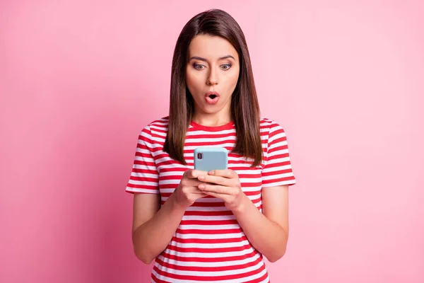 Retrato de una joven impresionada mirando fijamente teléfono ropa de boca abierta leer camiseta blanca aislada sobre fondo rosa — Foto de Stock