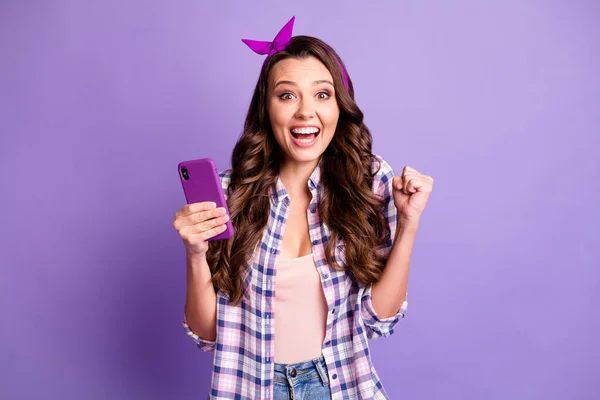 照片中疯狂的欣喜若狂的女孩用智能手机举起拳头穿着格子花衬衫，与紫色背景隔离 — 图库照片