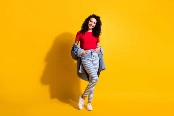 Full längd foto av söt flicka handflator fickor ser kamera bära röd topp randiga jeans jacka sneakers isolerad gul färg bakgrund — Stockfoto