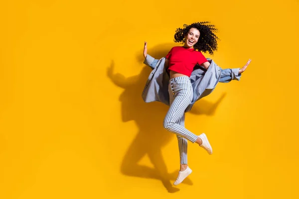 Volledige foto van meisje spring palmen dragen gestreepte jeans bijgesneden rode t-shirt jas sneakers geïsoleerde gele kleur achtergrond — Stockfoto