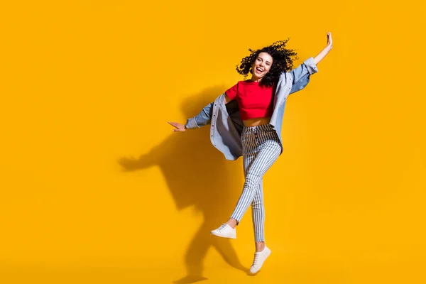 Full längd foto av dam hoppa höja ben händer bära randiga jeans beskärda röd t-shirt jacka sneakers isolerad gul färg bakgrund — Stockfoto