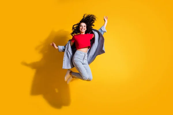 Full längd foto av dam hoppa hög vind hår bära randiga jeans beskärda röd t-shirt jacka sneakers isolerad gul färg bakgrund — Stockfoto