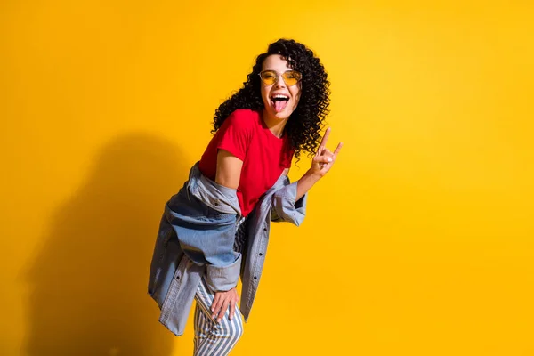 Foto de adorável jovem senhora tongue-out mostrar chifres desgaste vermelho t-shirt listrado jeans jaqueta vidro solar isolado cor amarela fundo — Fotografia de Stock