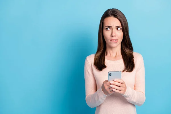 Retrato de ella que agradable atractiva chica de pelo castaño bastante preocupado utilizando dispositivo mirando a un lado espacio de copia morder labio aislado sobre brillante brillo vivo vibrante fondo de color azul —  Fotos de Stock