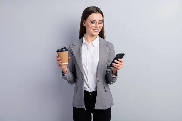 Foto de atractiva mujer de negocios confidente gerente trabajador mantener el teléfono leer noticias políticas bebida caliente fresco para llevar café ropa gafas camisa a cuadros chaqueta aislado color gris fondo — Foto de Stock