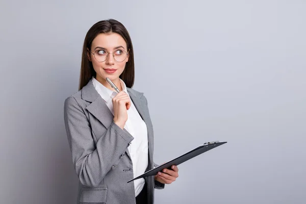 Foto de atractiva mujer de negocios gerente distancia remota sujetar portapapeles lápiz pensar creativo nombre del artículo periodista usar especificaciones camisa a cuadros chaqueta aislado color gris fondo — Foto de Stock