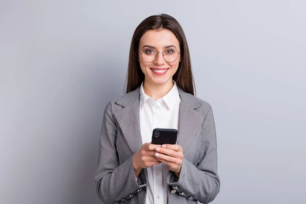 Photo of attractive business lady pewnie kierownik pracownik trzymać telefon ręce czytać wiadomości polityczne toothy uśmiechnięty zużycie specs koszula blezer odizolowany szary kolor tła — Zdjęcie stockowe