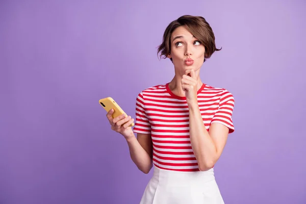 Foto de menina bonito segurar telefone mão queixo lábios olhar para cima espaço vazio desgaste listrado t-shirt isolado roxo cor fundo — Fotografia de Stock