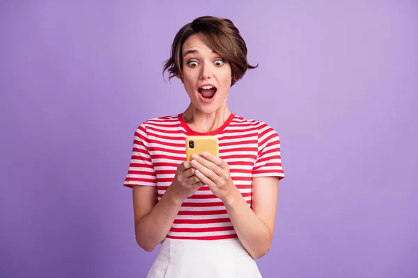 Photo of crazy lovely lady hold smartphone look screen open mouth wear striped t-shirt isolated purple color background