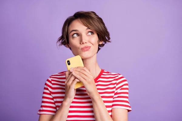 Zdjęcie z przemyślane słodkie pani trzymać telefon patrzeć puste miejsce nosić paski t-shirt odizolowany fioletowy kolor tła — Zdjęcie stockowe