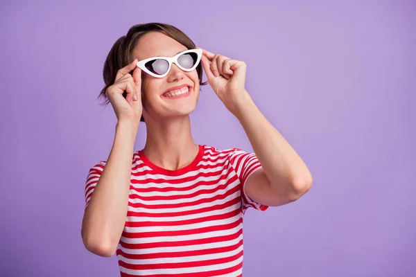 Foto av söt flicka hålla glasögon ser tomt utrymme glänsande leende bära solglasrandig t-shirt isolerad lila färg bakgrund — Stockfoto