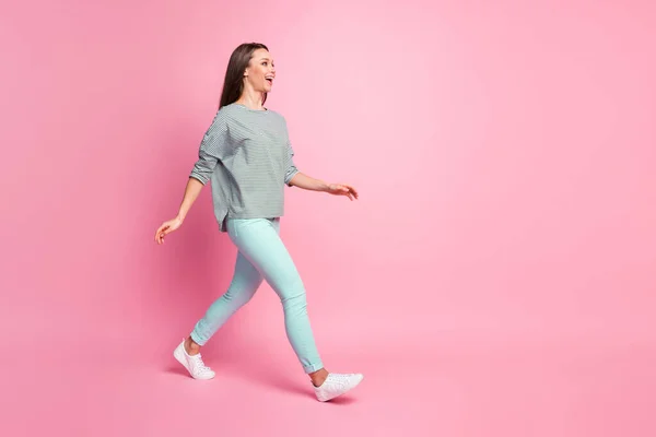 Foto de perfil de tamaño completo de la mujer bonita optimista que va a usar pantalones azules zapatillas de deporte camisa aislada sobre fondo de color rosa — Foto de Stock