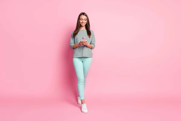 Full size foto van optimistische mooie jonge vrouw gaan kijken telefoon dragen blauwe jeans sneakers trui geïsoleerd op roze achtergrond — Stockfoto