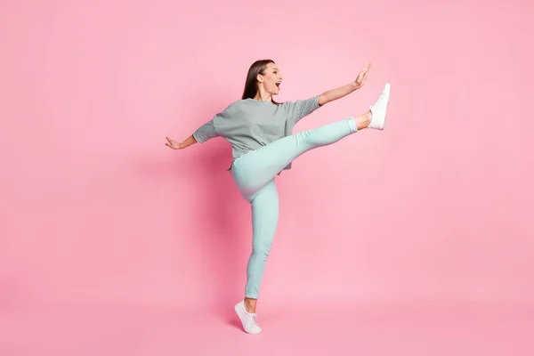 Foto de perfil de tamaño completo de la joven divertida sorprendida bailando pierna arriba usar pantalones de camisa zapatillas aisladas sobre fondo de color rosa pastel — Foto de Stock