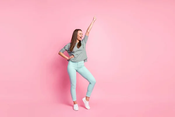 Full size photo of optimistic funky young woman dancing hand up wear shirt pants sneakers isolated on pastel pink color background — Stock Photo, Image