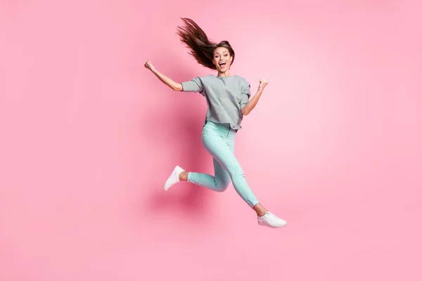 Full size photo of cheerful astonished girl jumping hands fists wear shirt pants sneakers isolated on pastel pink color background — Stock Photo, Image