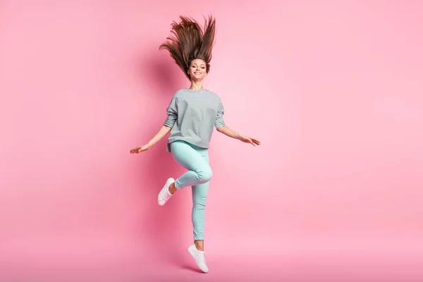 Foto de tamaño completo de chica linda optimista salto pierna pelo largo hasta usar pantalones de la camisa zapatillas aisladas sobre fondo de color rosa pastel — Foto de Stock