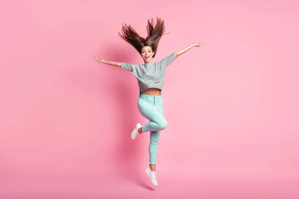 Teljes méretű fotó optimista megdöbbent lány ugró kéz fel kopás ing kék nadrág fehér tornacipő elszigetelt rózsaszín szín háttér — Stock Fotó