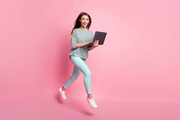 Foto de perfil em tamanho completo de otimista engraçado morena cabelo menina correr salto digitando laptop usar calças de camisa tênis isolado no fundo rosa — Fotografia de Stock