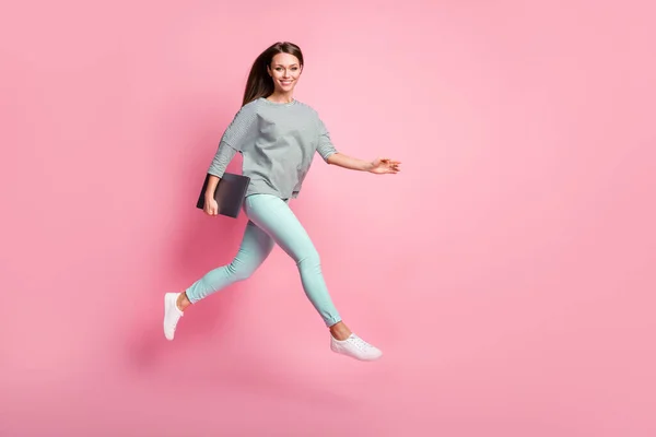 점프하는 쾌활하고 달콤 한 갈색 소녀의 전체 크기 프로필 사진 휴대용 노트북 셔츠 스니커즈 핑크 색 배경에 분리 — 스톡 사진