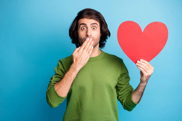 Fotografie bláznivý ohromený chlap představující srdce forma ruka zavřít ústa nosit zelený svetr izolované modré barvy pozadí — Stock fotografie