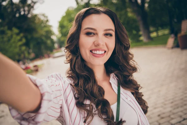 Foto portrét ženské vlivné s hnědé vlnité vlasy přičemž selfie vesele se usmívá na ležérní bílé pruhované košile v městském parku — Stock fotografie