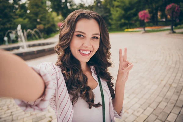 Foto portrét ženy blogger s brunetkou kudrnaté vlasy přičemž selfie s úsměvem ukazující V-znamení gesto mír se dvěma prsty — Stock fotografie