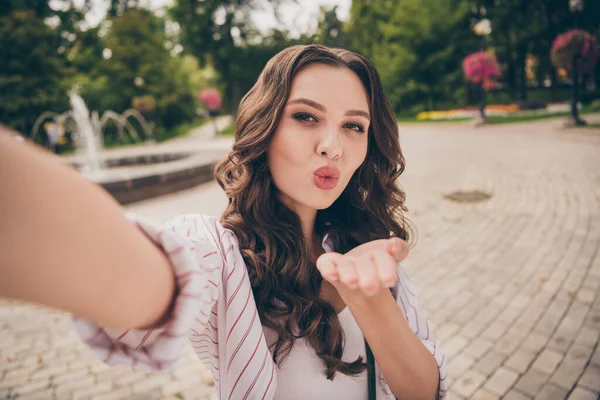 Photo portrait of female blogger with brunette curly hair taking selfie sending air kiss with plump pouted lips wearing casual clothes