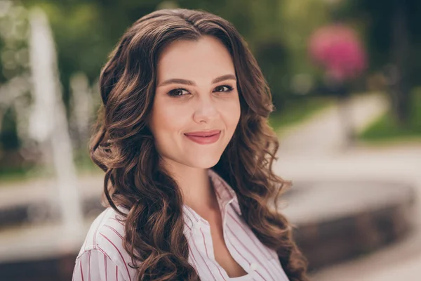 Portrait photo d'une jolie fille timide avec une coiffure bouclée souriante portant une chemise décontractée blanche avec des rayures marchant dans un parc de printemps vert — Photo