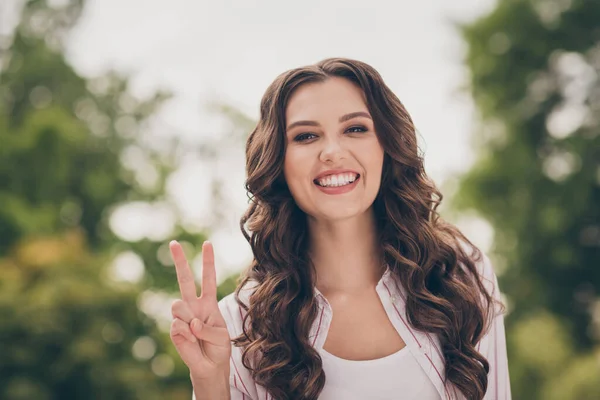 Portrait photo de belle jeune femme avec coiffure bouclée marchant dans un parc d'été montrant un geste de signe en V avec deux doigts — Photo