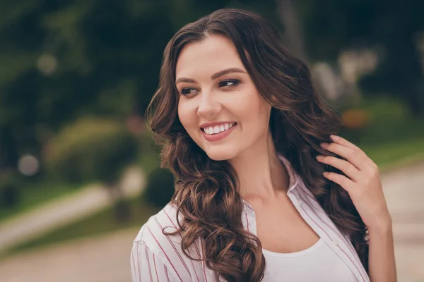 Foto porträtt av söt kvinnlig student röra brunett hår leende tittar på sidan promenader i den gröna stadsgatan — Stockfoto