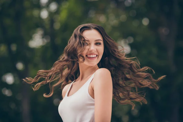 Фото милой милой молодой женщины улыбающейся имеют длинные вьющиеся брюнетки волосы пешком парк носить белый топ на открытом воздухе — стоковое фото