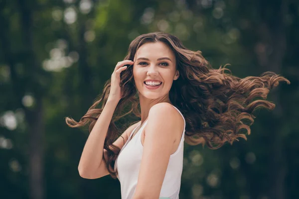 Foto de agradável bonito jovem mulher sorrindo toque longo encaracolado morena cabelo andando parque desgaste branco superior ao ar livre — Fotografia de Stock