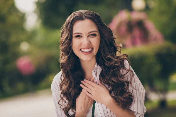 Retrato de adorable linda morena pelo largo rizado joven dama manos pecho usar rayas camisa caminar fuera —  Fotos de Stock