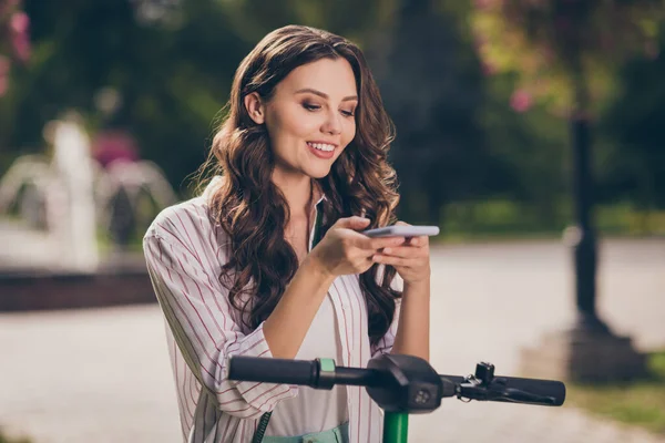 Фото красивых оптимистичных вьющихся волос юная леди сканировать сегвей по телефону носить полосатую рубашку наслаждаться весенним свежим воздухом на улице — стоковое фото