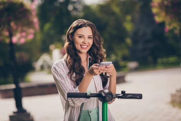 Foto van charmante tevreden dame met behulp van telefoon en paardrijden kick-scooter — Stockfoto