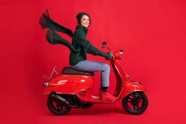 Boczny profil pełna długość portret atrakcyjnej osoby jazdy motorower X-mas wycieczka dżinsy buty izolowane na czerwonym tle kolor — Zdjęcie stockowe