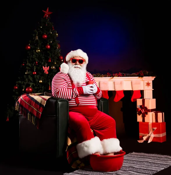 Noel Baba 'nın oturduğu sandalyenin resmi. Kap bacakları sıcak. Havza, x-mas kostüm gözlükleri takın. — Stok fotoğraf