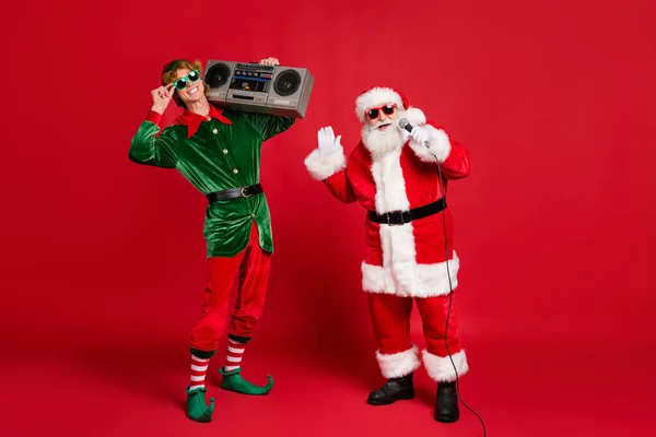 Foto de dois homens funky elfo segurar rádio retro santa segurar microfone cantar desgaste x-mas traje capa de vidro solar isolado fundo cor vermelha — Fotografia de Stock
