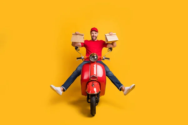 Zdjęcie nieostrożny szalony facet jazdy rower trzymać dwa opakowania nosić czerwony t-shirt czapka jeansy izolowane żółty kolor tło — Zdjęcie stockowe