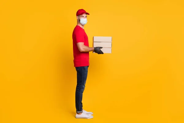 Profilo foto di corriere uomo contenere pacchi scatole indossare guanti maschera rosso t-shirt cap jeans scarpe da ginnastica isolato colore giallo sfondo — Foto Stock
