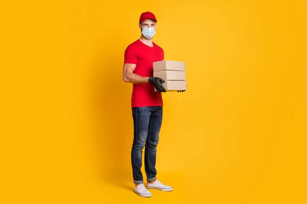 Foto di giovane tenere tre scatole di carta indossare maschera rosso t-shirt copricapo jeans scarpe da ginnastica isolato colore giallo sfondo — Foto Stock