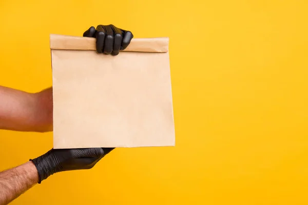 Cropped photo of delivery man bras tenir emporter paquet de papier porter des gants noirs isolés fond de couleur jaune vif — Photo