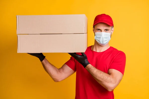 Фото хлопця, що тримає доставку, демонструє дві великі коробки в рукавичках маска червона футболка капелюх ізольований жовтий кольоровий фон — стокове фото