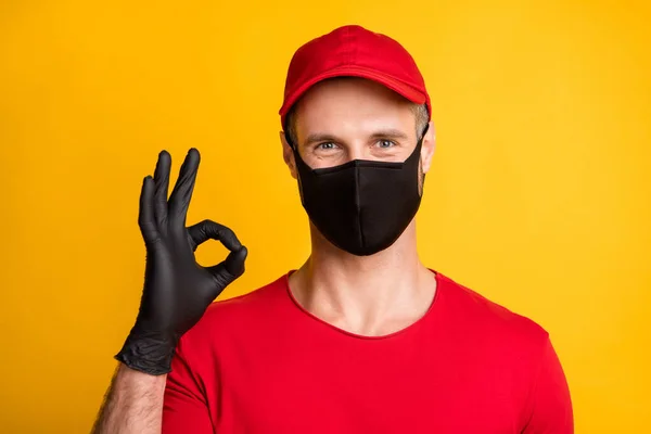 Fotografie klidného pošťáka demonstrovat prsty okey znamení nosit masku červené tričko klobouk izolované žluté barvy pozadí — Stock fotografie