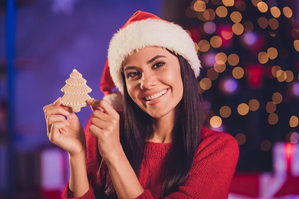 Zdjęcie młodej atrakcyjnej pięknej uśmiechniętej wesołej kobiety nosić kapelusz Świętego Mikołaja trzymać nowy rok ciasteczko herbatnik w domu — Zdjęcie stockowe