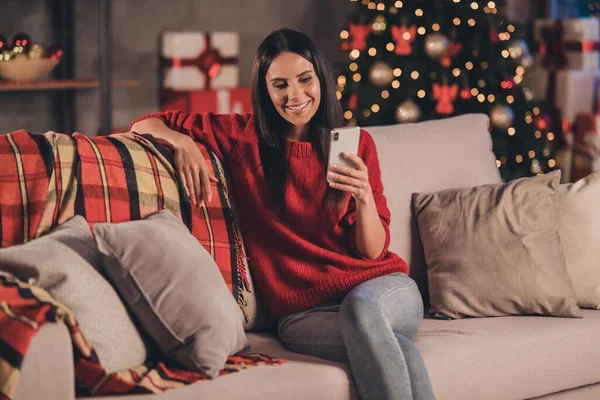 Zdjęcie młodej atrakcyjnej pięknej uśmiechniętej dobrej nastroju pozytywnej pogodnej kobiety siedzieć na kanapie wpisując sms na smartfonie w domu — Zdjęcie stockowe