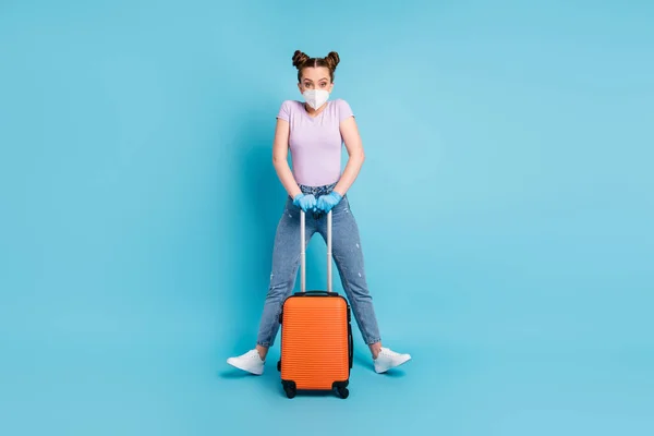 Foto de corpo inteiro de senhora bonita usar respirador passar check-aeroporto segurar caso rolante voar para casa pais controle viral humor brincalhão desgaste t-shirt jeans sapatos luvas isolado azul cor fundo — Fotografia de Stock