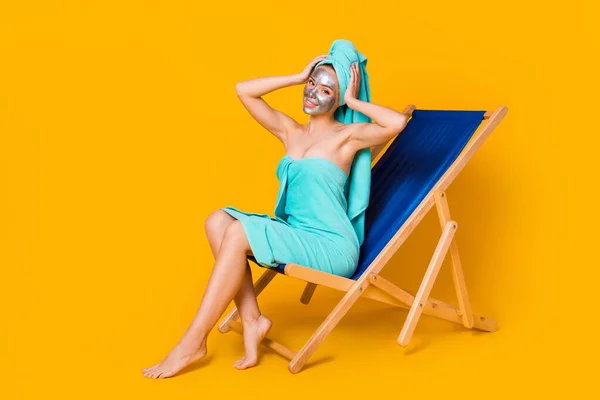 Foto corpo pieno di giovane donna sedersi chaise-longue godere di trattamento viso mani toccare la testa isolata su sfondo di colore giallo — Foto Stock